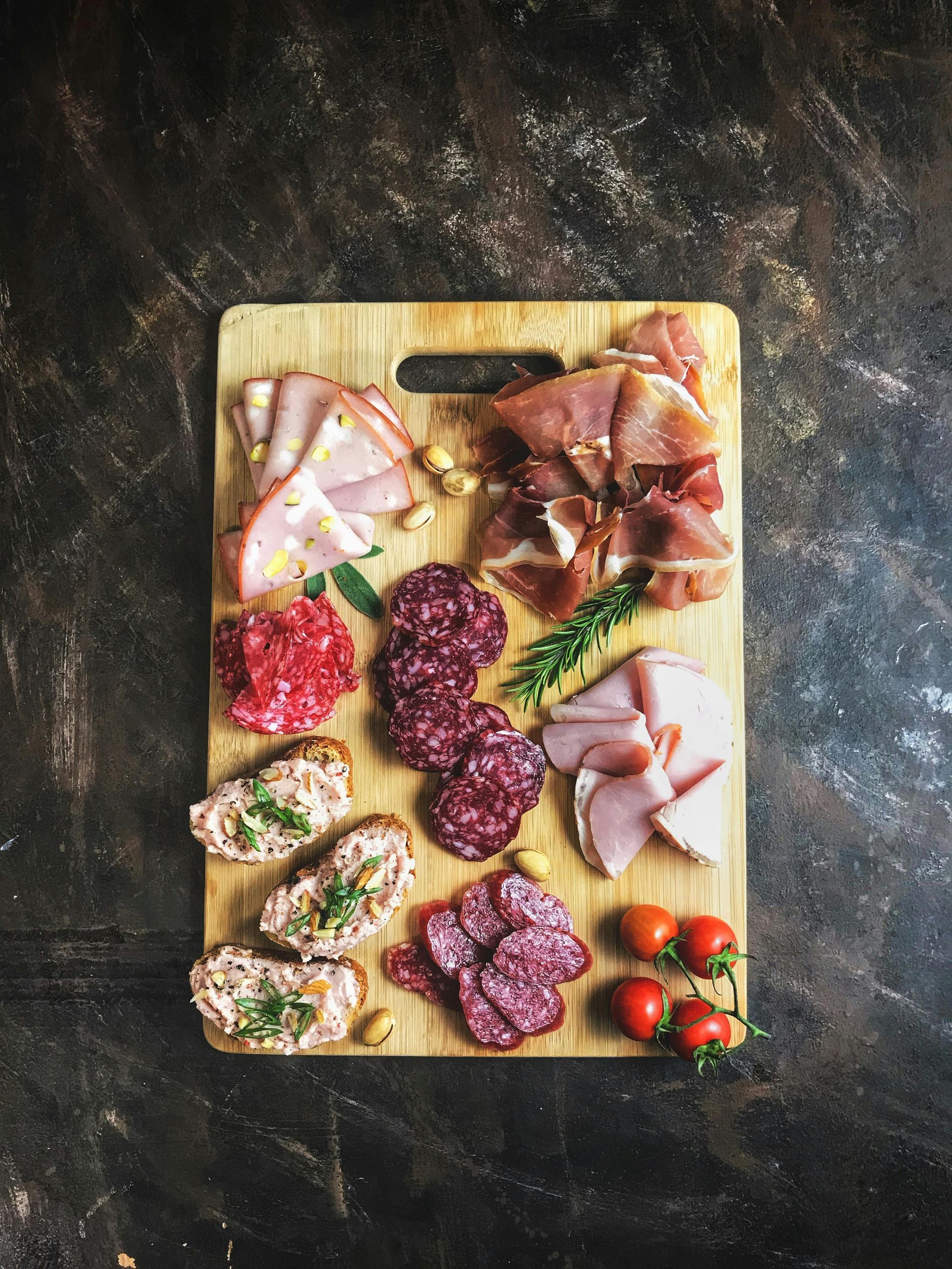 Charcuterie board with various sliced meats, tomatoes, and appetizers on a wooden board.