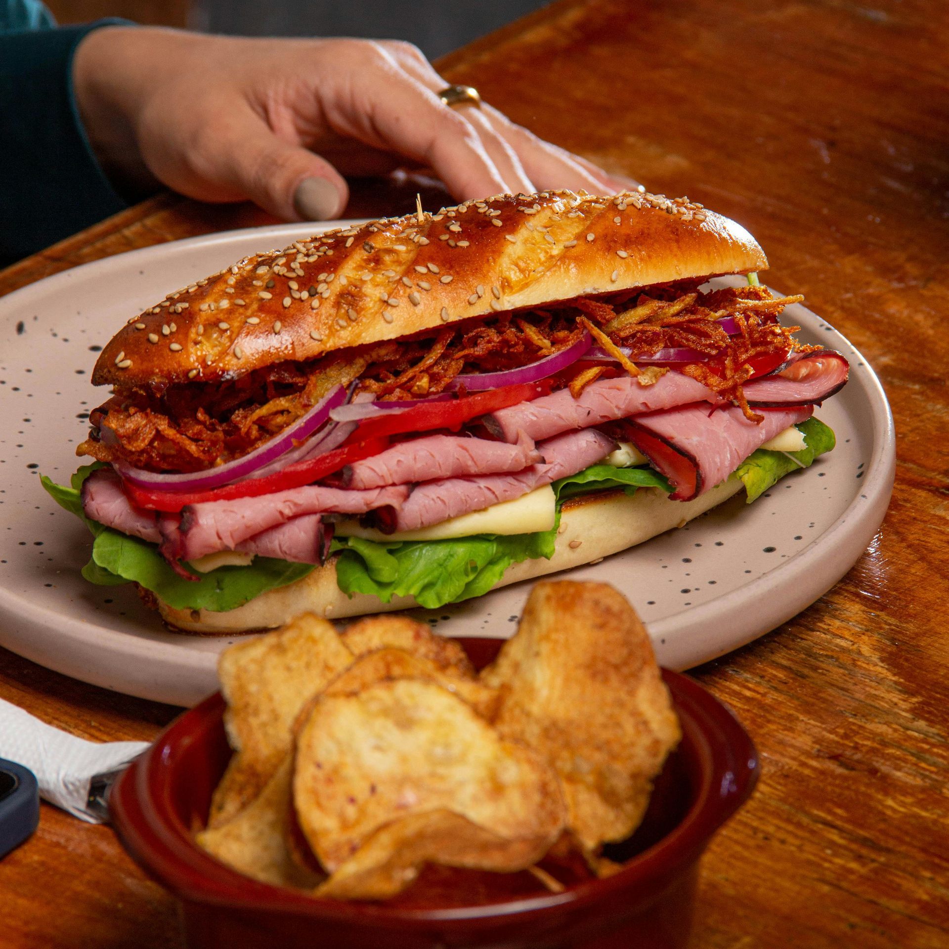 Sub sandwich with roast beef, red onion, and fried onions on a plate with chips.