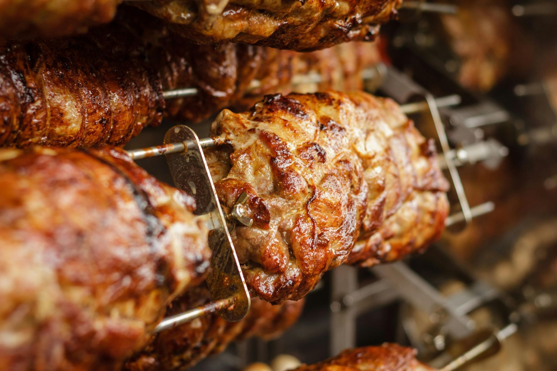 Rotisserie chicken roasting on a metal spit, golden-brown skin, close-up.