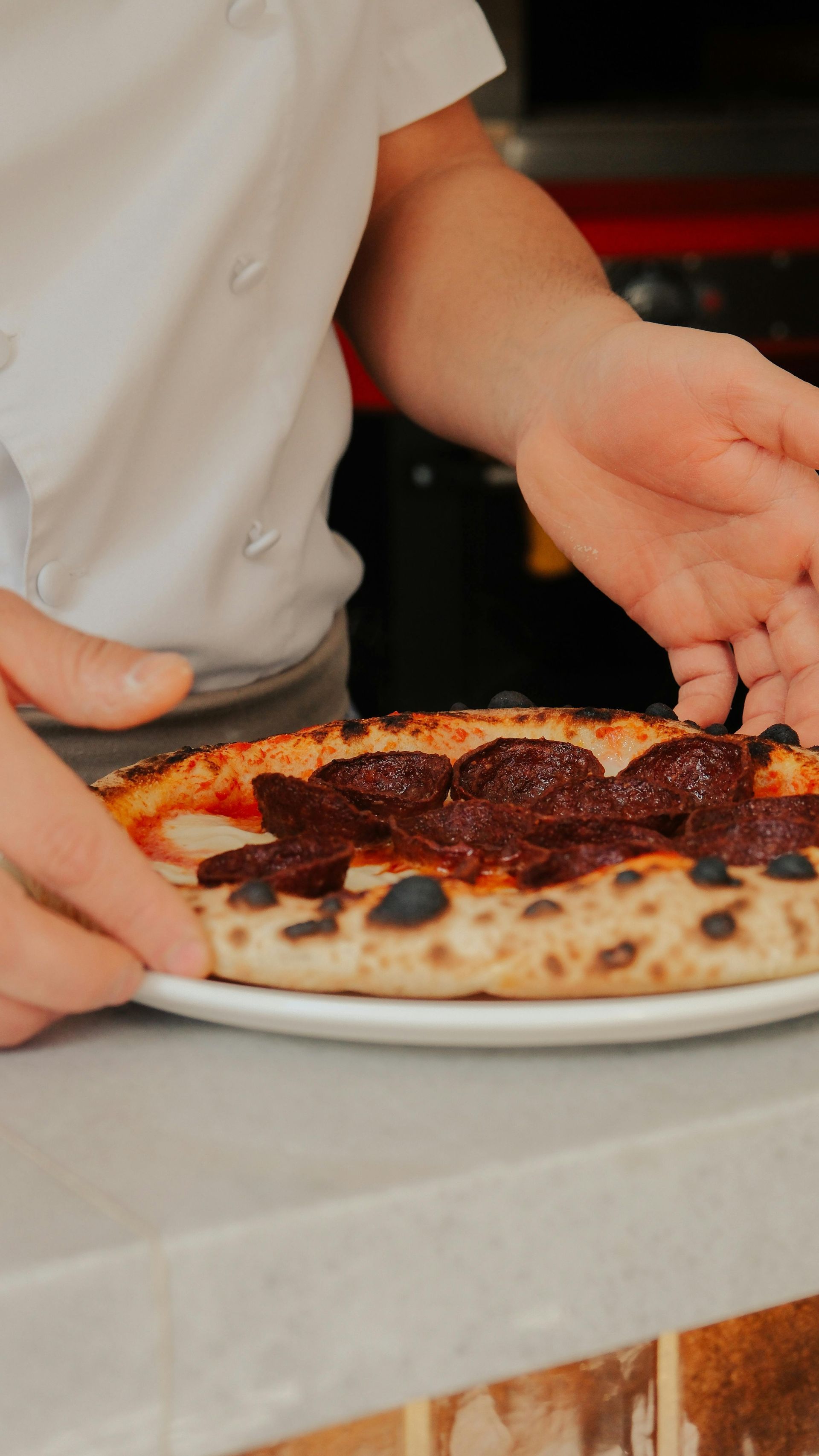 Chef placing a pizza with dark toppings on a plate. Kitchen setting.
