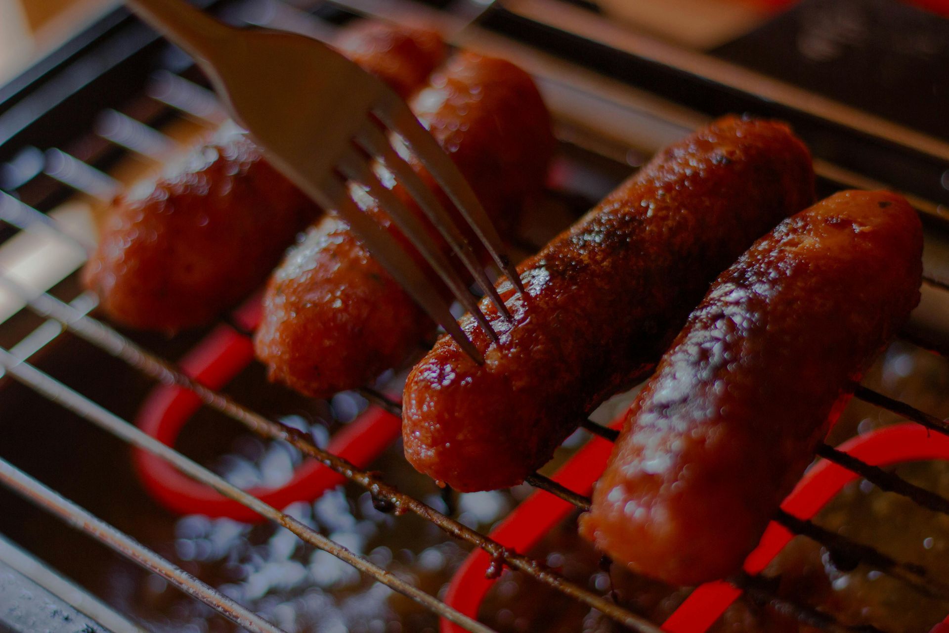 Sausages grilling on an electric griddle, being pierced by a fork.