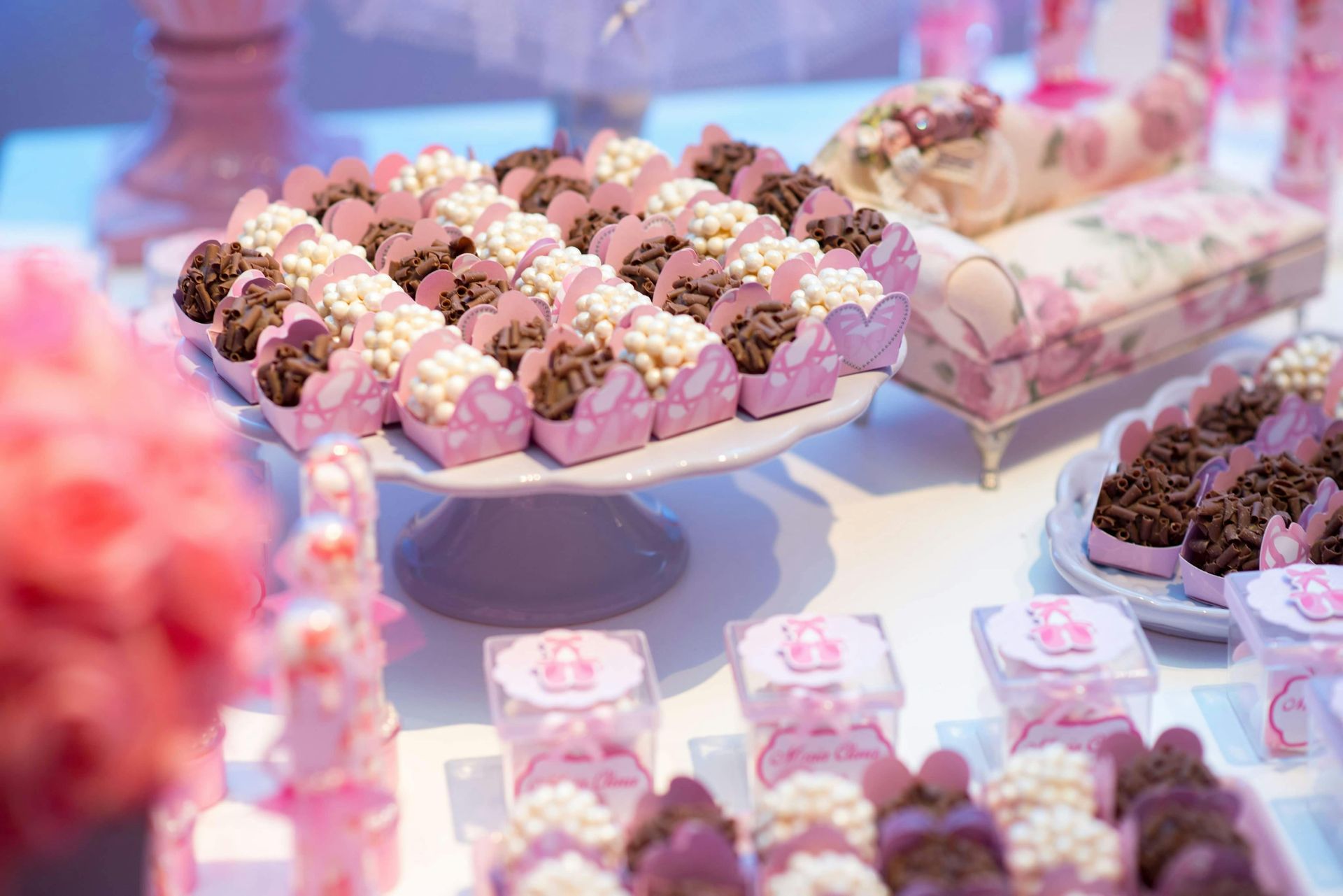 Dessert table with pink-themed treats: cakes, candies, and a decorative chaise lounge.