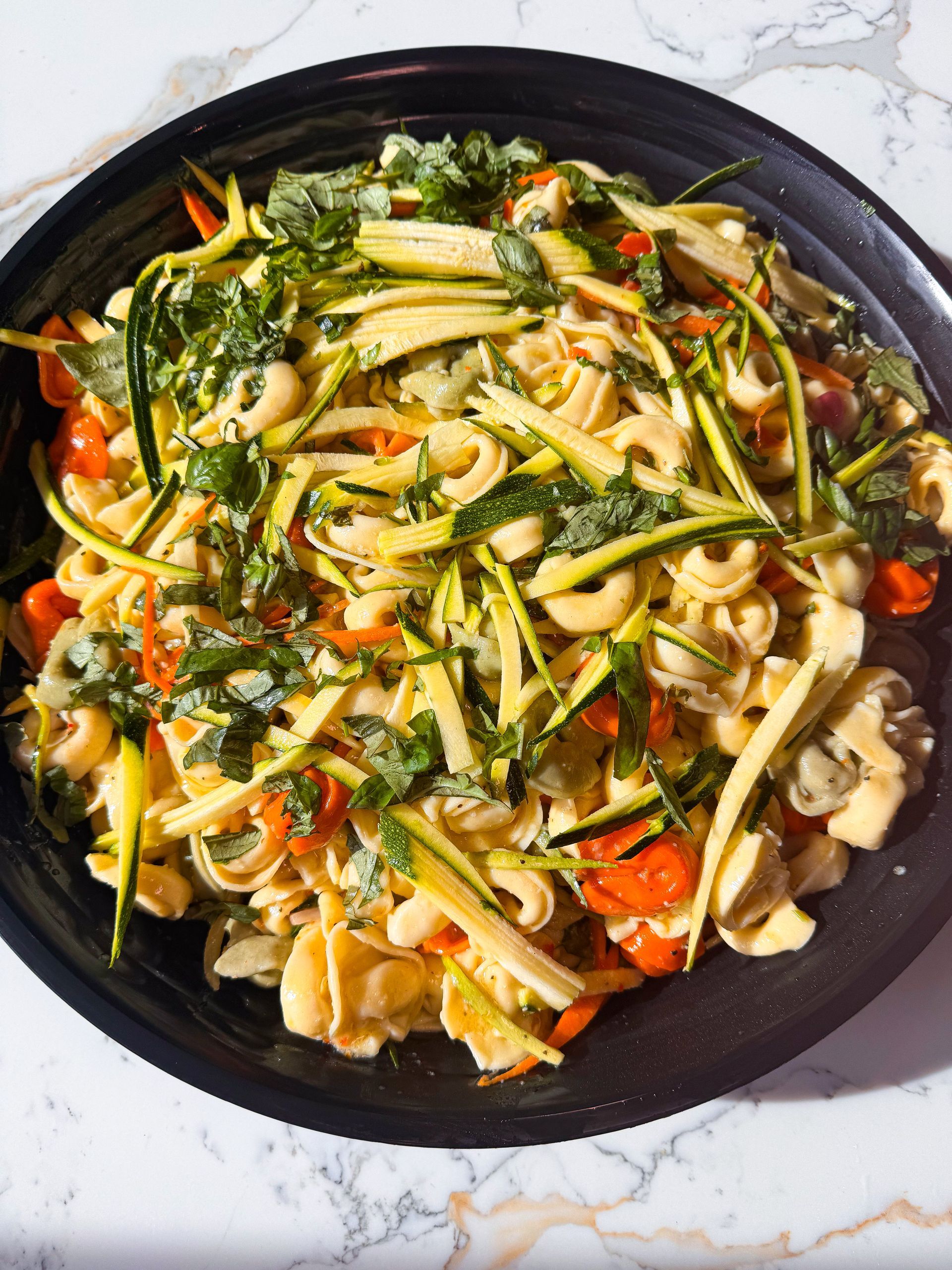 Pasta salad with zucchini, cherry tomatoes, and parsley in a black bowl.