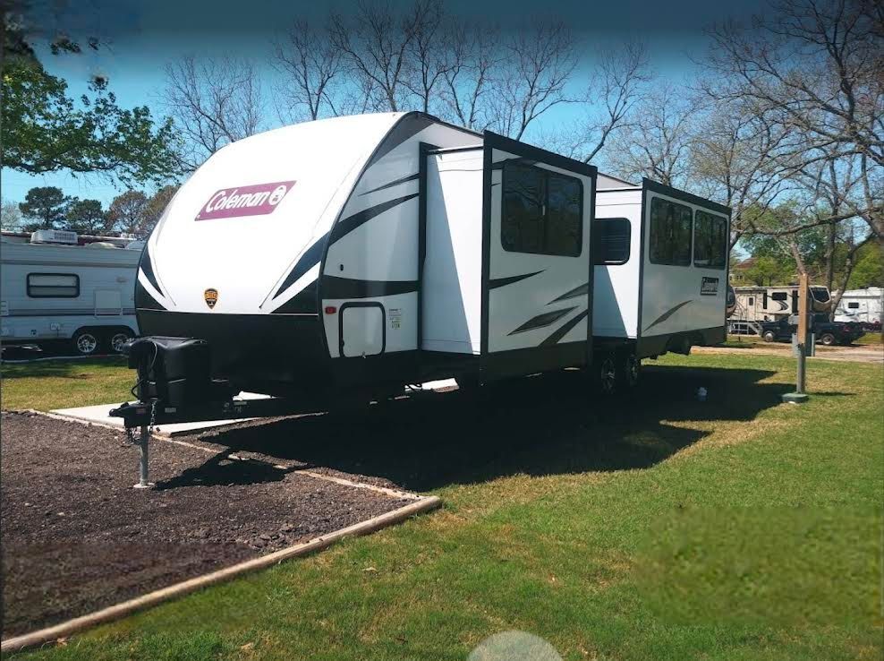 A white and black coleman trailer is parked in a grassy area.