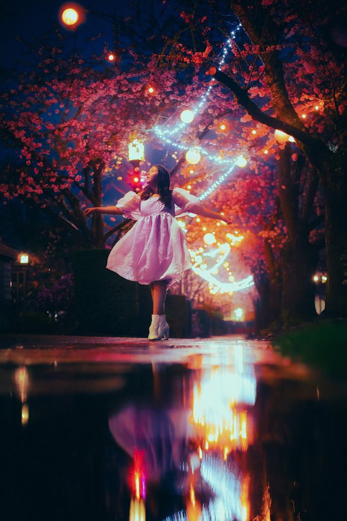 A woman in a white dress is dancing in front of a cherry blossom tree.