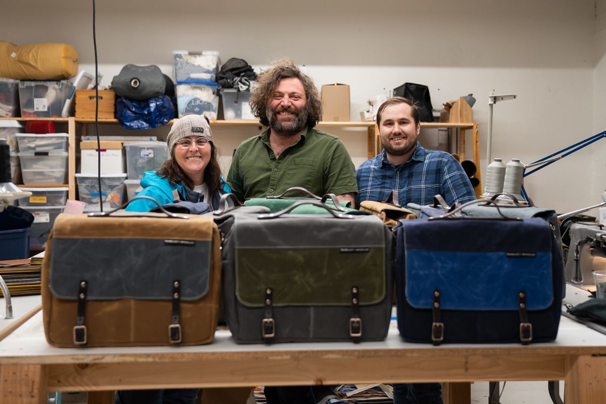 A group of people are standing around a table with bags on it.