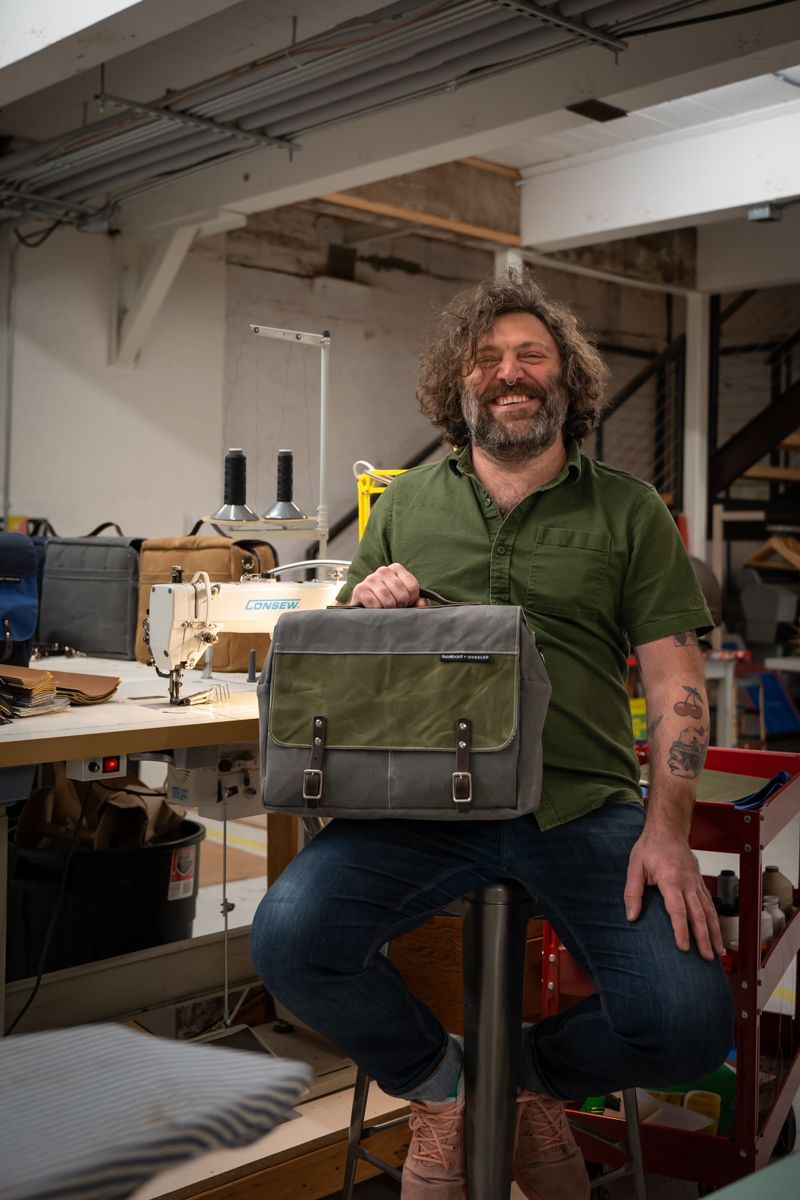 A man is sitting on a stool in a factory holding a bag.