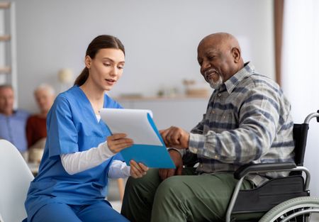 A nurse is talking to an elderly man in a wheelchair.