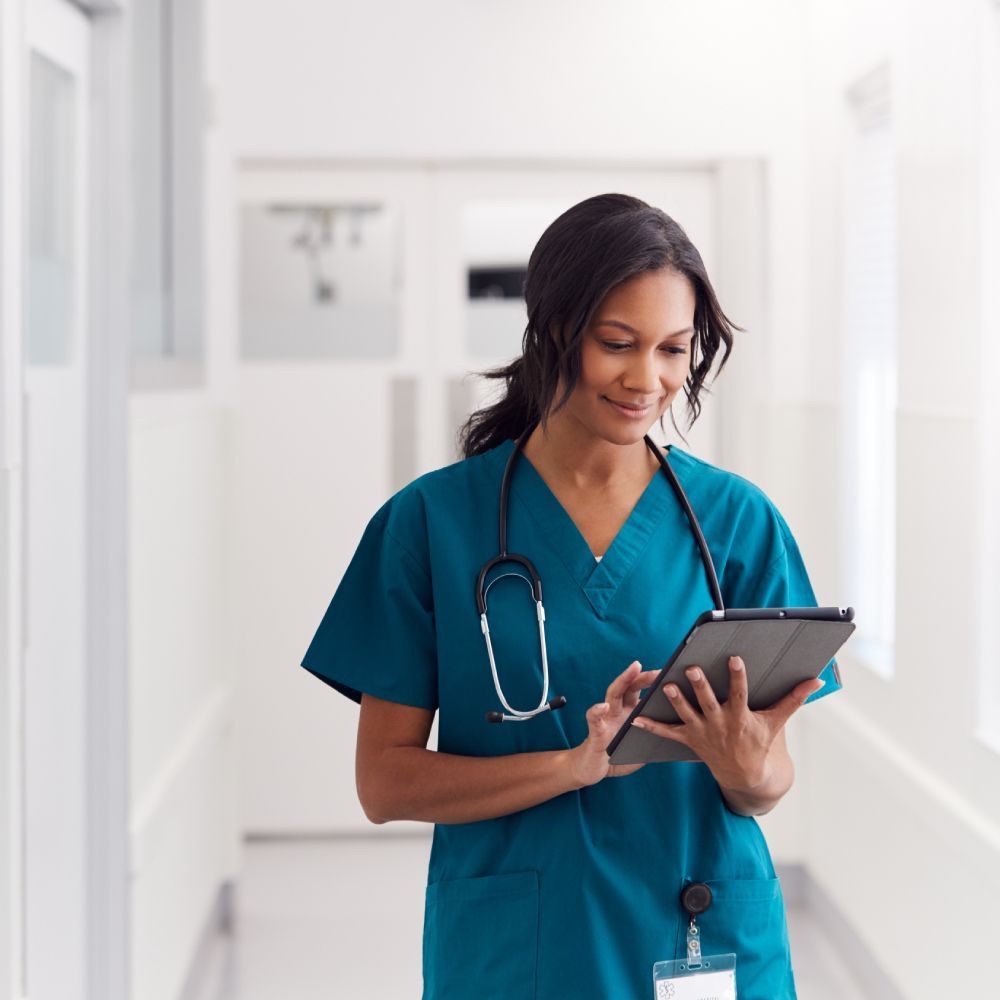 A nurse is using a tablet in a hospital hallway.