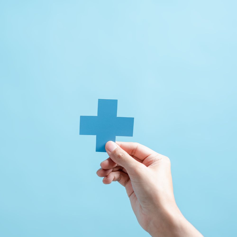 A hand is holding a blue paper cross on a blue background.