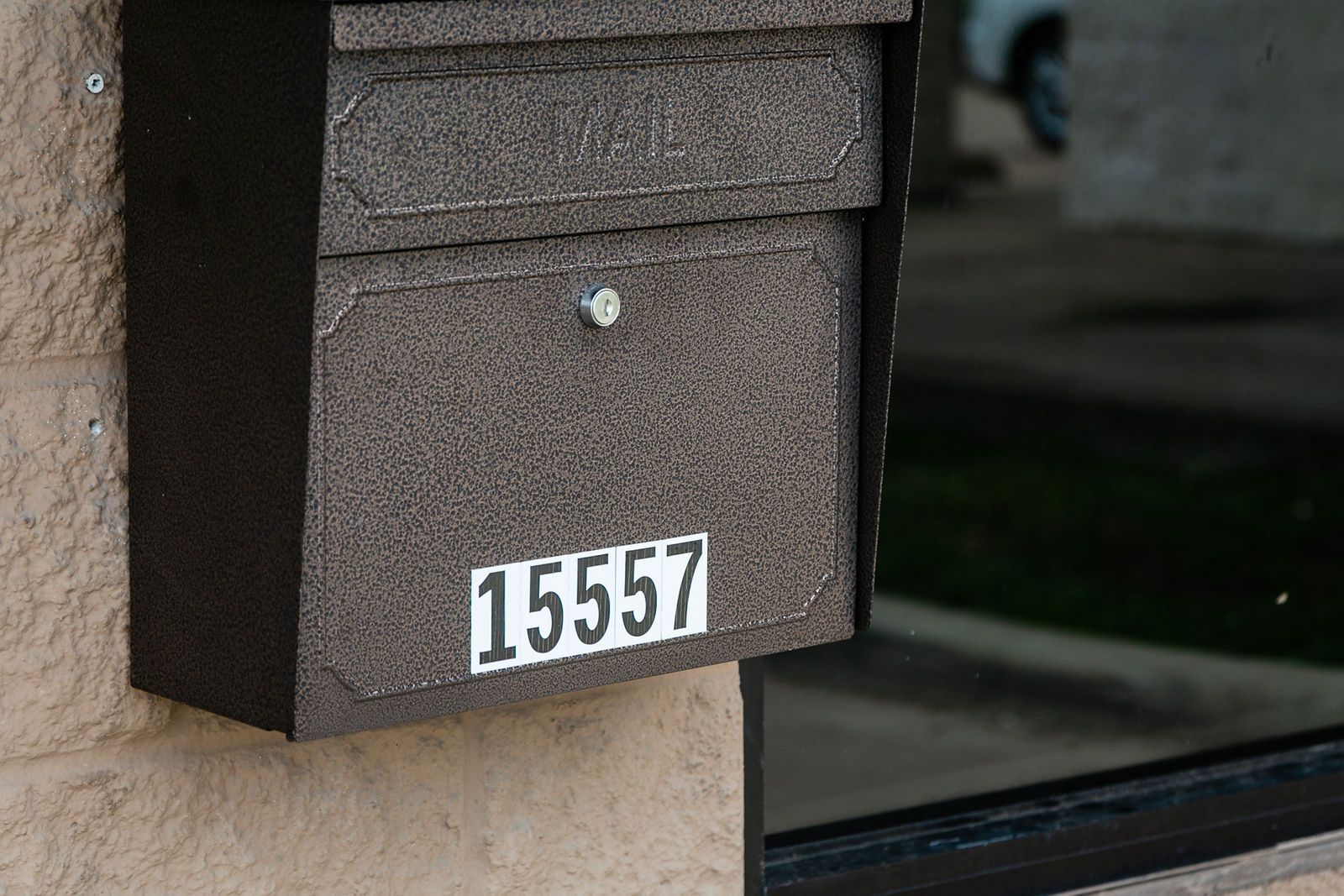 A dark, textured metal mailbox mounted on a beige brick wall, featuring the white number 15557 on the front. | 2 QuickAuto, Car & Tire Repair | Copperfield