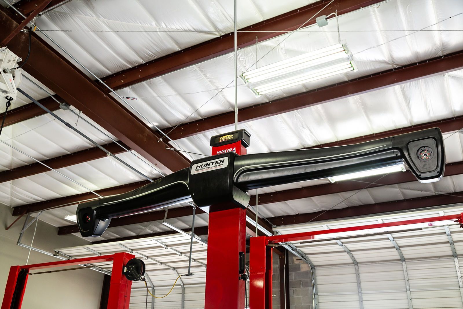A black overhead sensor bar mounted on a red support column in a garage with a white metal ceiling. | 2 QuickAuto, Car & Tire Repair | Copperfield