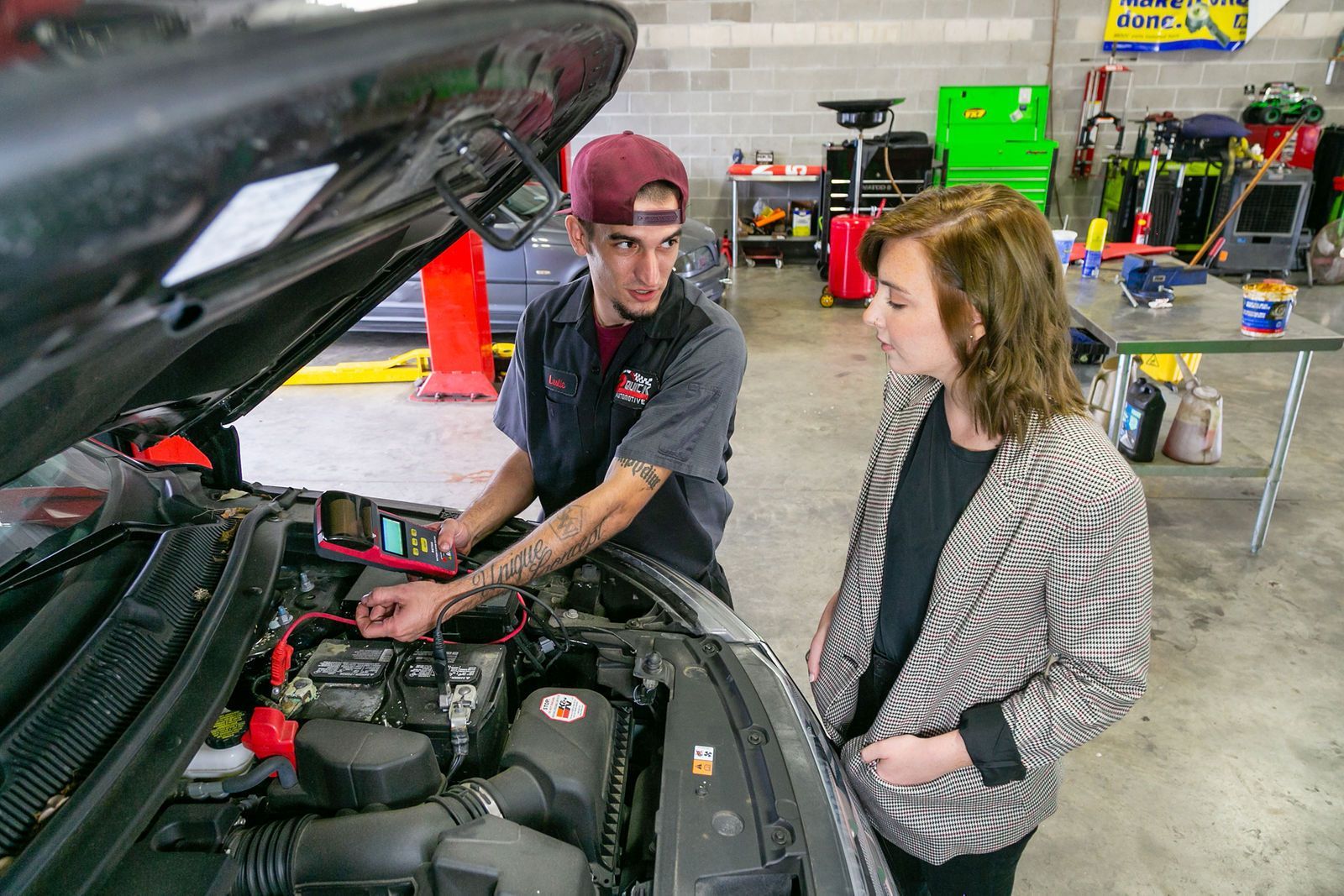 A technician explains a vehicle engine component to a person while standing in an automotive repair shop. | 2 QuickAuto, Car & Tire Repair | Copperfield