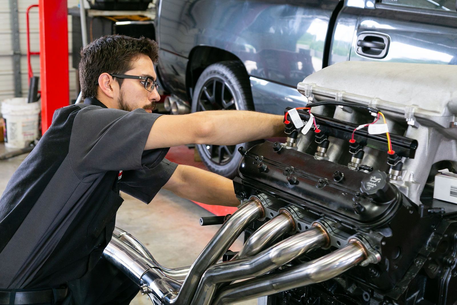 A mechanic works on a car engine in a garage, focusing intently while adjusting components on the engine block. | 2 QuickAuto, Car & Tire Repair | Copperfield