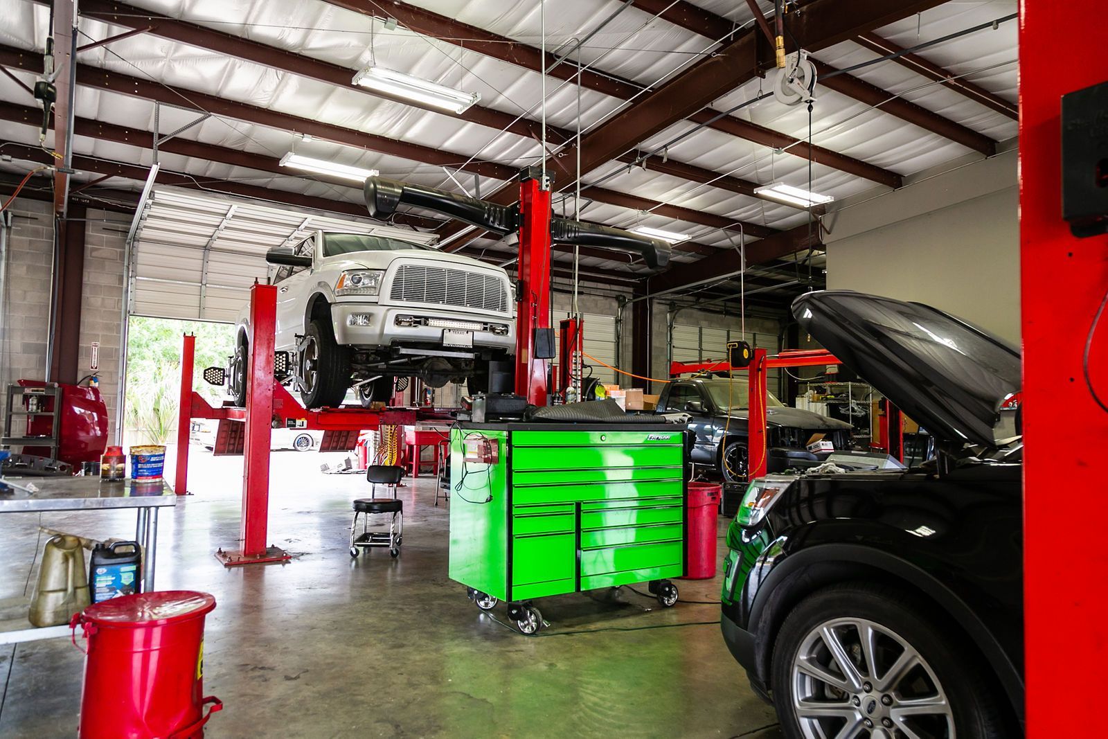 A bright auto repair shop featuring a white truck raised on a lift, a green toolbox, and a black car with its hood up. | 2 QuickAuto, Car & Tire Repair | Copperfield