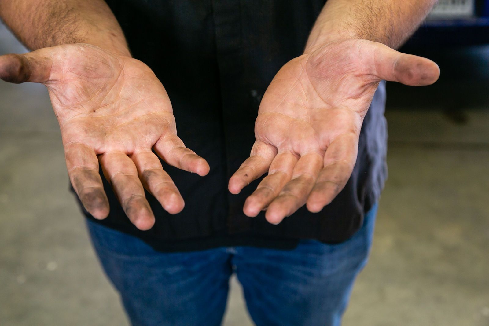 A person in a black shirt showing their palms and fingertips covered in dark grease, suggesting manual or mechanical work. | 2 QuickAuto, Car & Tire Repair | Copperfield