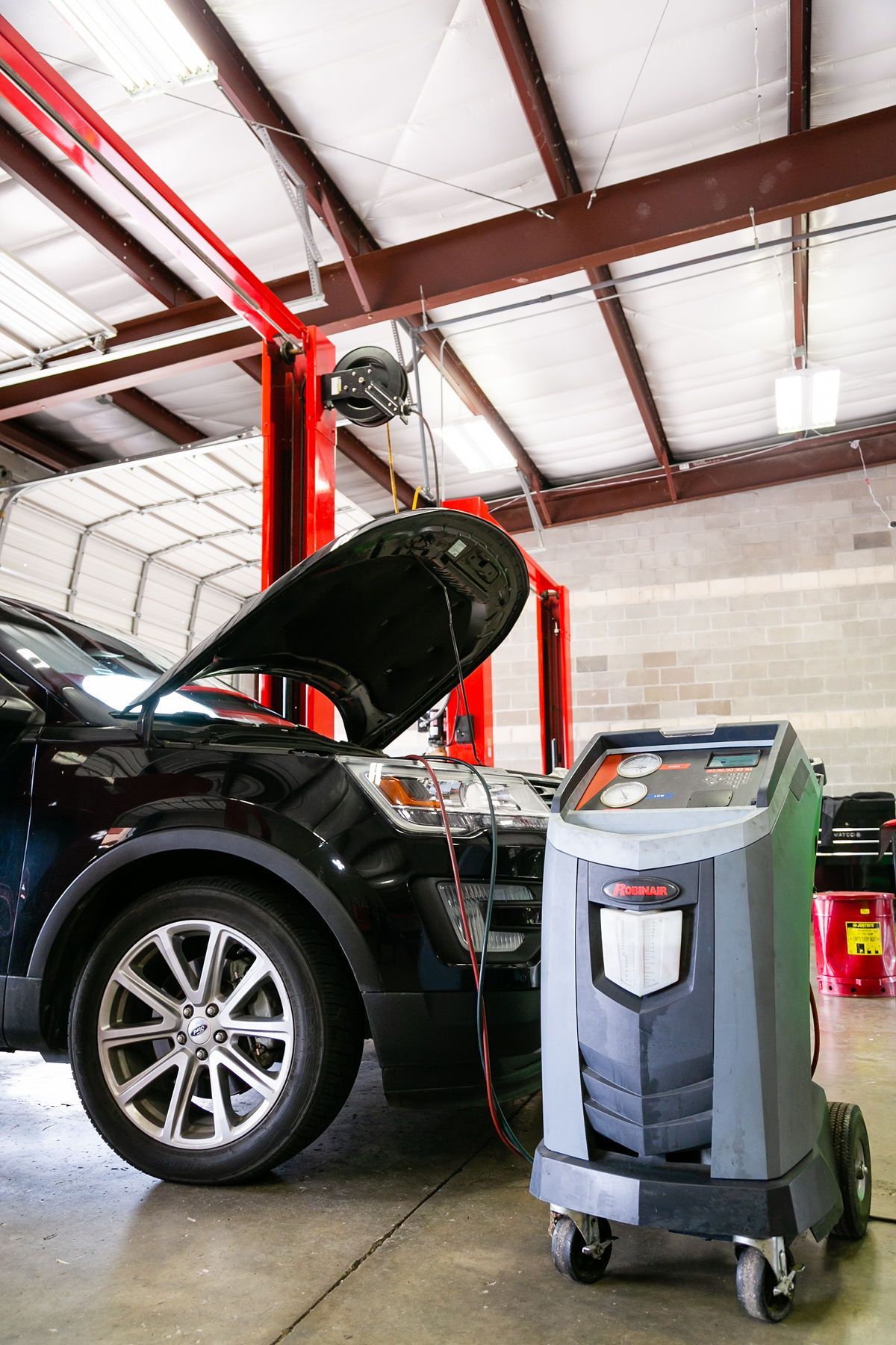 A black car with an open hood in a repair shop connected to a gray A/C service machine on wheels. | 2 QuickAuto, Car & Tire Repair | Copperfield