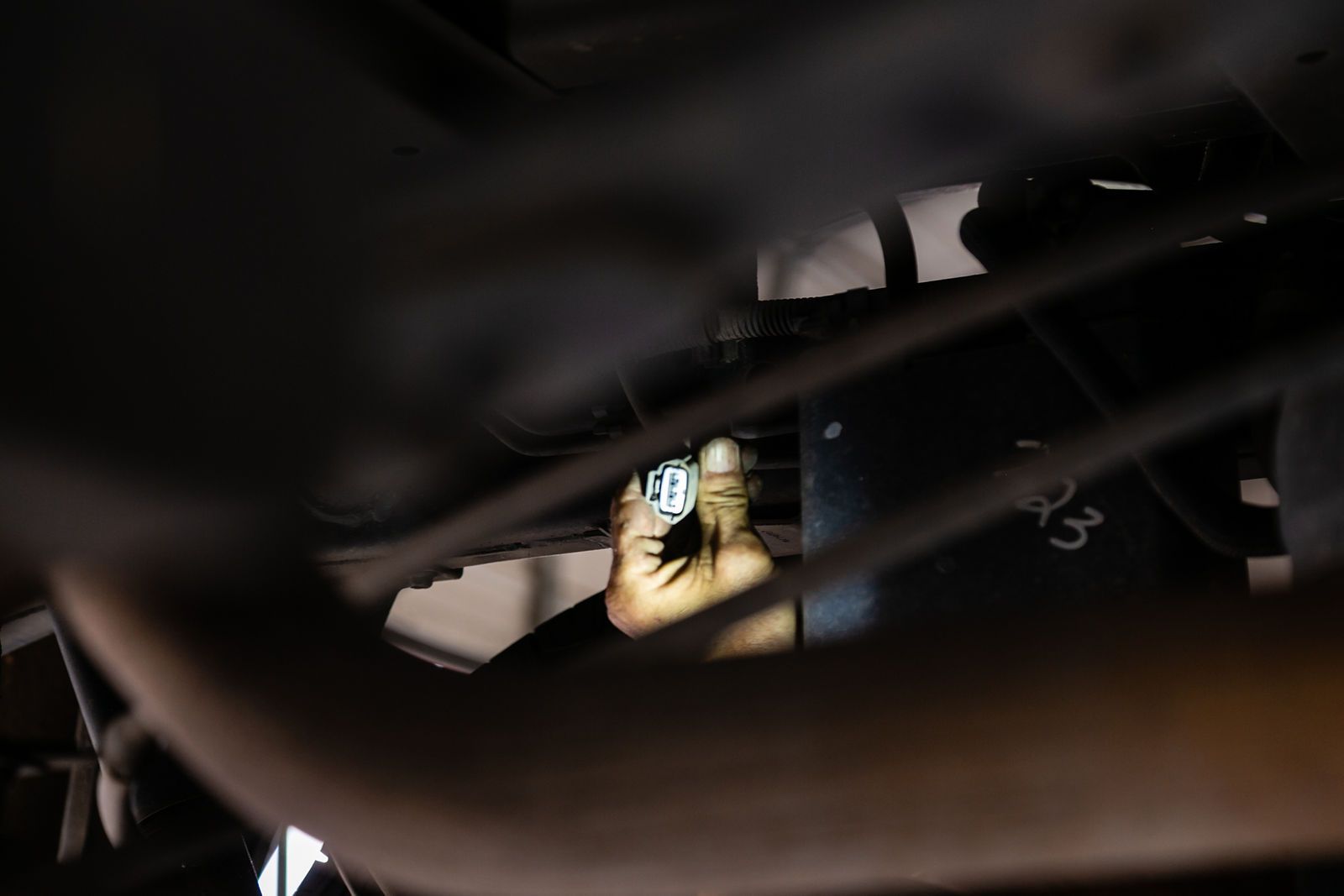 A hand under the chassis of a vehicle, holding and plugging in an electrical wiring harness connector. | 2 QuickAuto, Car & Tire Repair | Copperfield