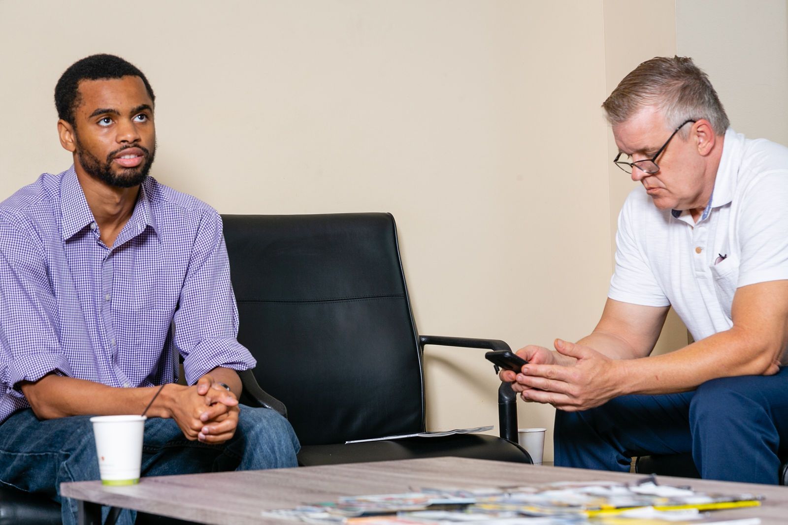Two men sit in a waiting room; one looks forward while the other looks down at his phone. | 2 QuickAuto, Car & Tire Repair | Copperfield