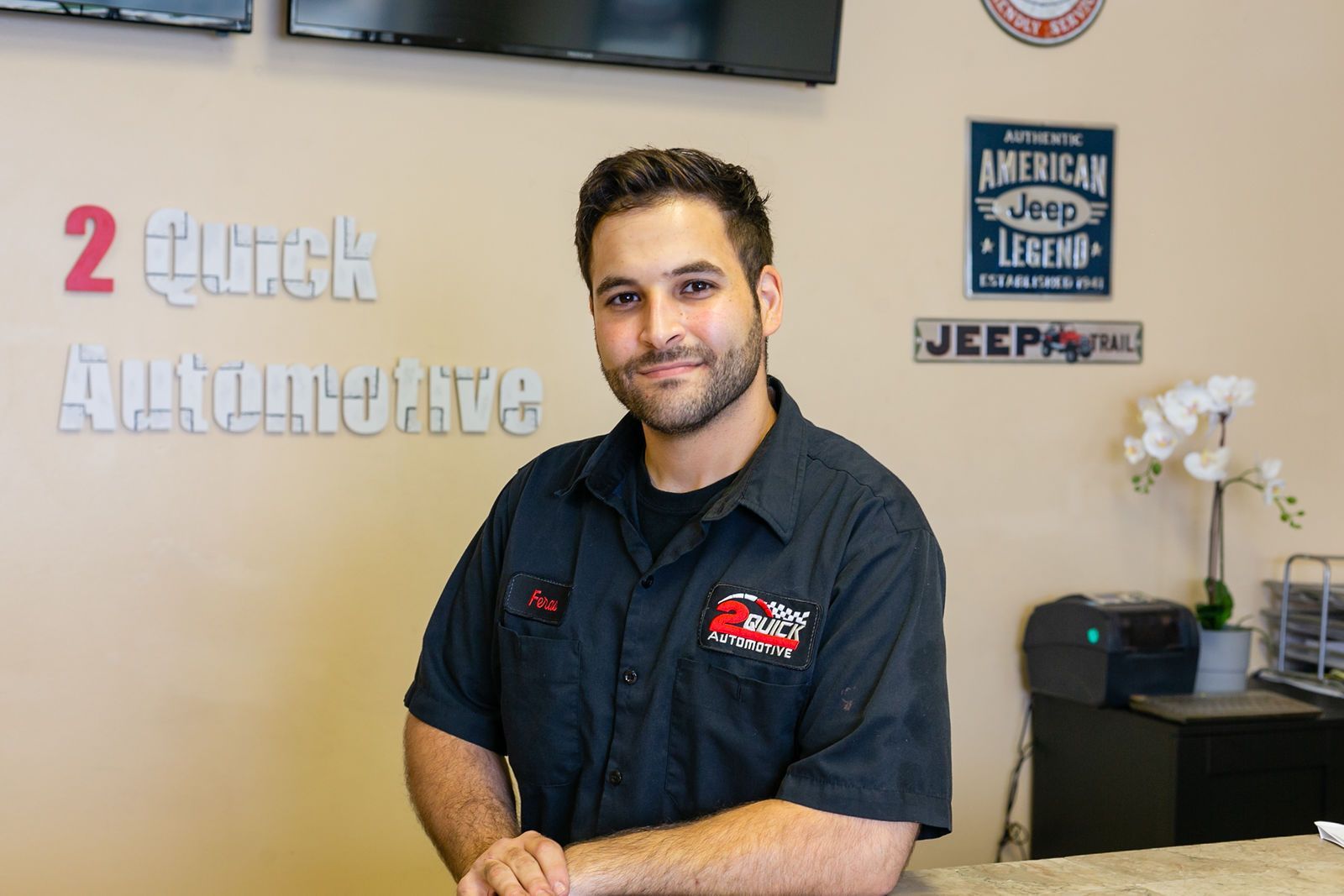 A person wearing a dark uniform shirt smiles in front of a wall with 