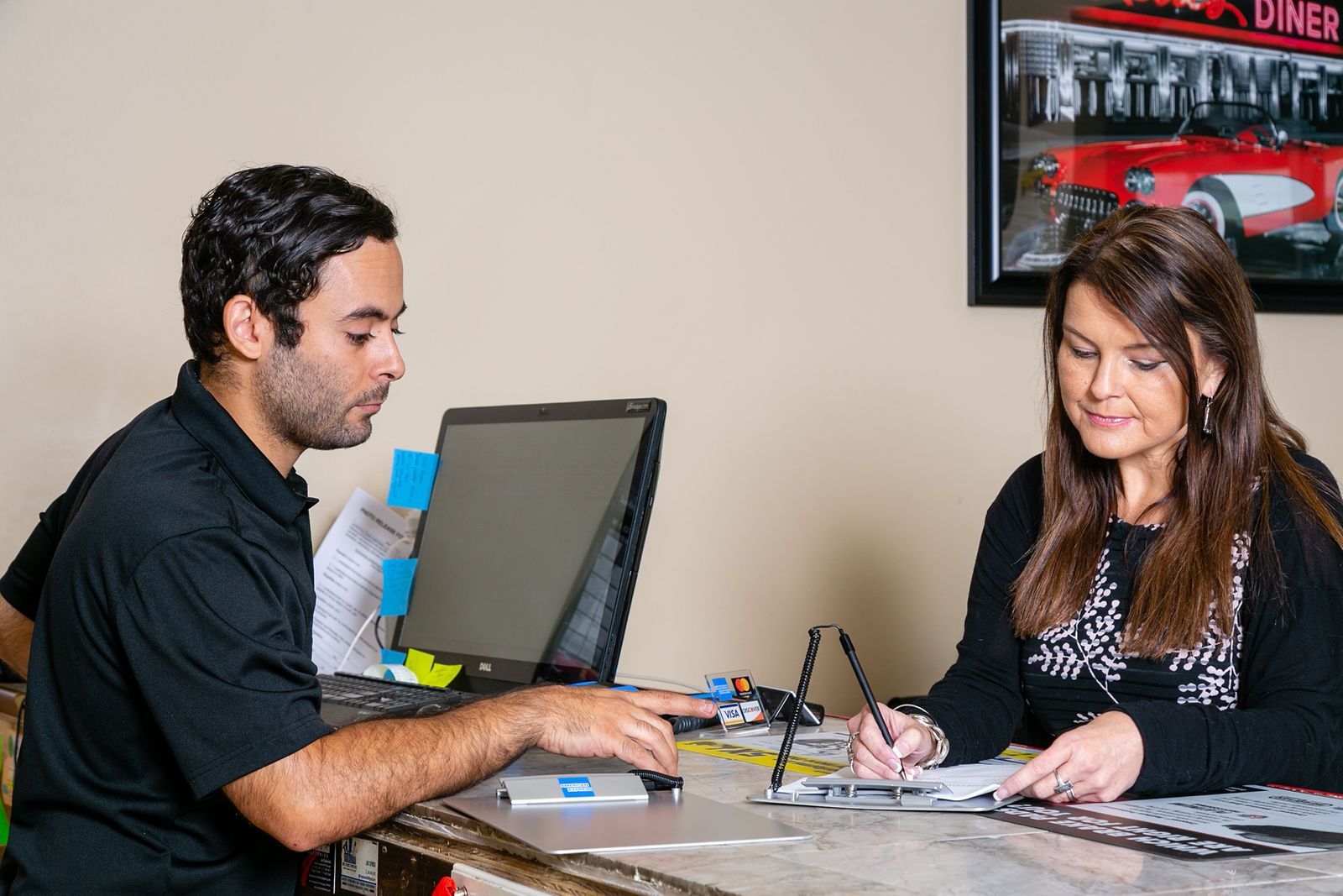 Two professionals sit at a desk, reviewing documents and working on a computer in an office setting. | 2 QuickAuto, Car & Tire Repair | Copperfield