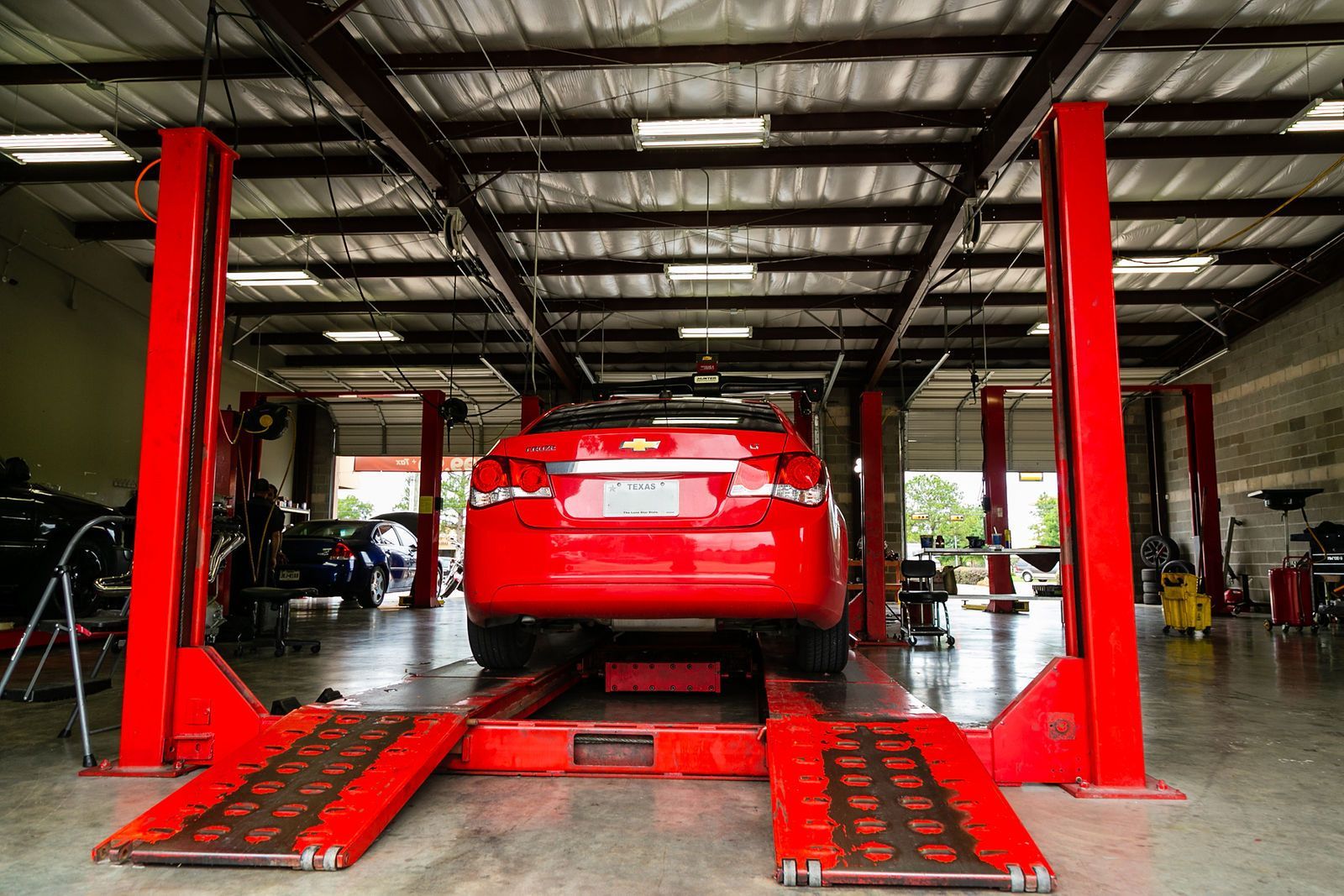 A red car positioned on a red auto lift inside a brightly lit automotive repair shop. | 2 QuickAuto, Car & Tire Repair | Copperfield