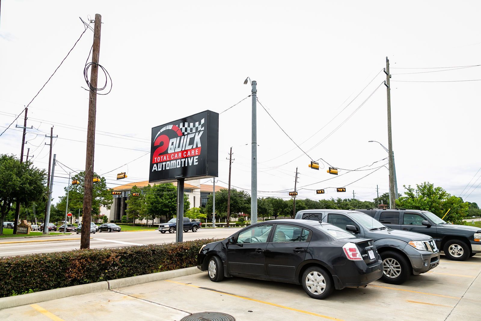 A black sign for 2 Rock Automotive stands in a parking lot with a black sedan and SUV parked on a concrete surface. | 2 QuickAuto, Car & Tire Repair | Copperfield