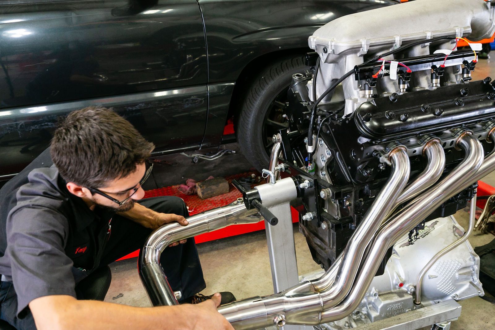A technician in a garage works on a large, high-performance car engine mounted on a stand. | 2 QuickAuto, Car & Tire Repair | Copperfield
