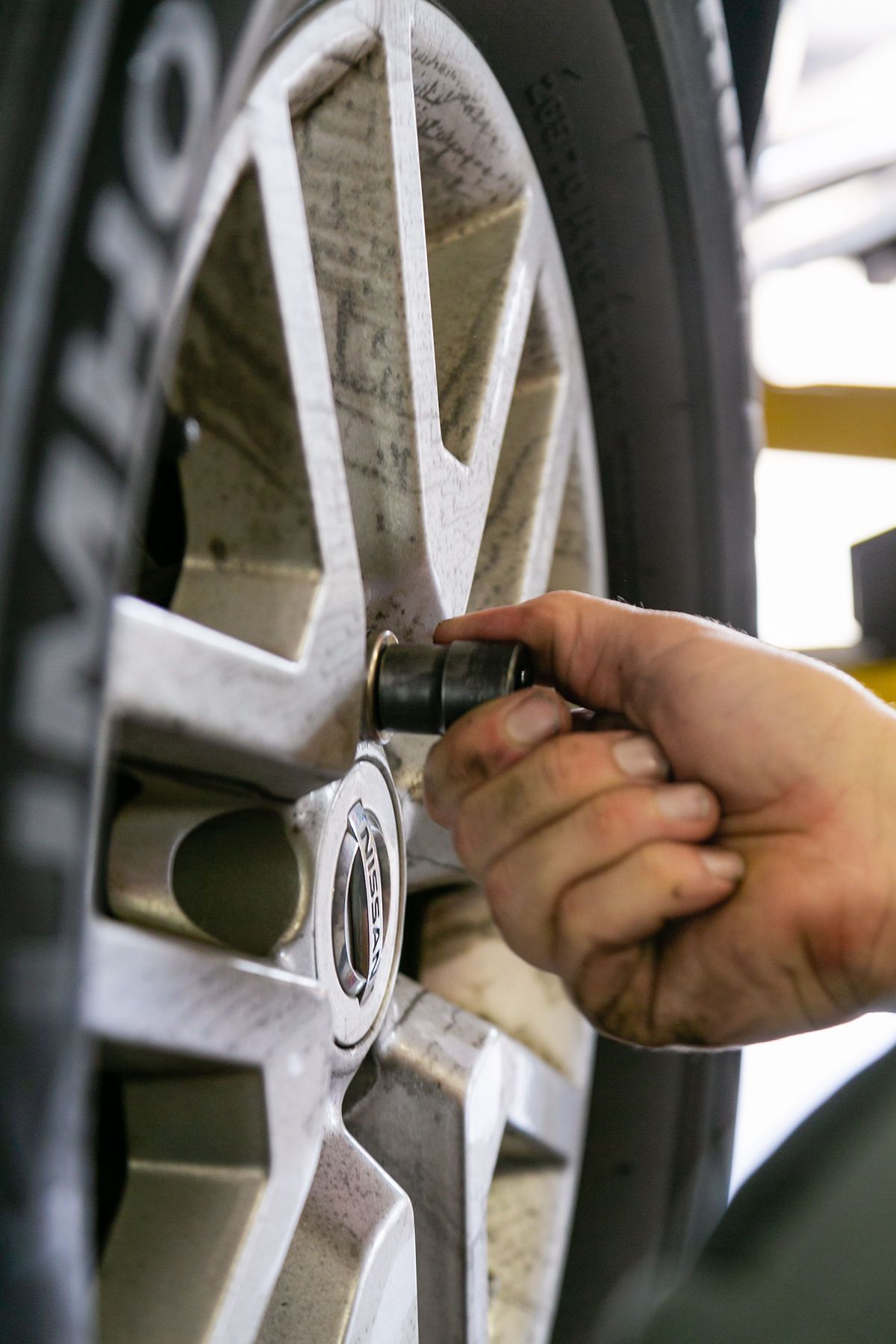 A close-up of a hand tightening a lug nut on a vehicle's tire rim with a socket tool in a repair shop setting. | 2 QuickAuto, Car & Tire Repair | Copperfield