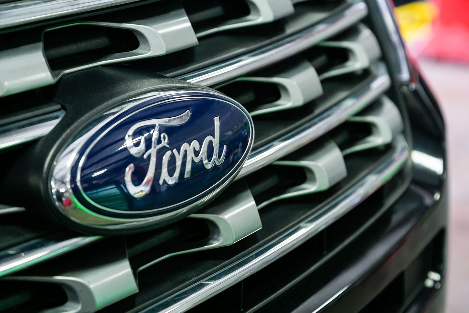 Close-up of a blue Ford logo emblem mounted on a dark, multi-slatted metallic car grille. | 2 QuickAuto, Car & Tire Repair | Copperfield