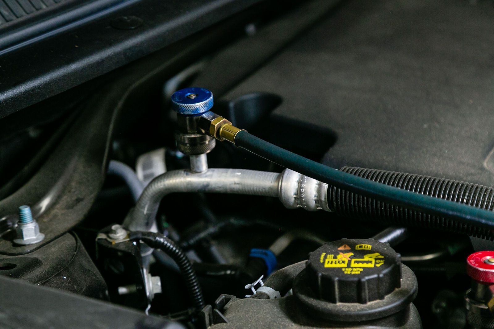 A blue hose connected to a valve on a car's air conditioning system inside an engine bay. | 2 QuickAuto, Car & Tire Repair | Copperfield