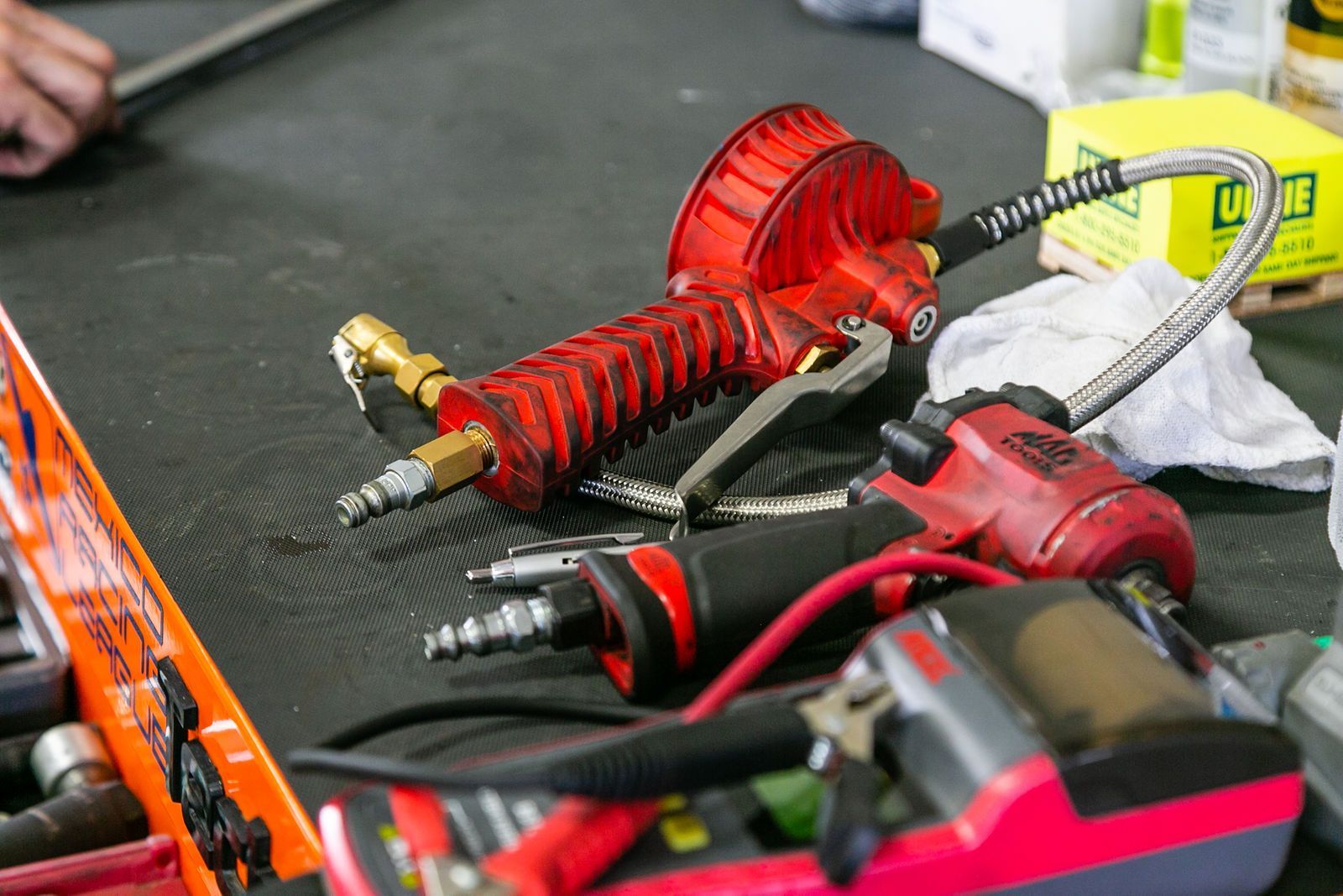 A red pneumatic tool with a hose, alongside a red impact wrench and other shop tools, on a black workshop mat. | 2 QuickAuto, Car & Tire Repair | Copperfield