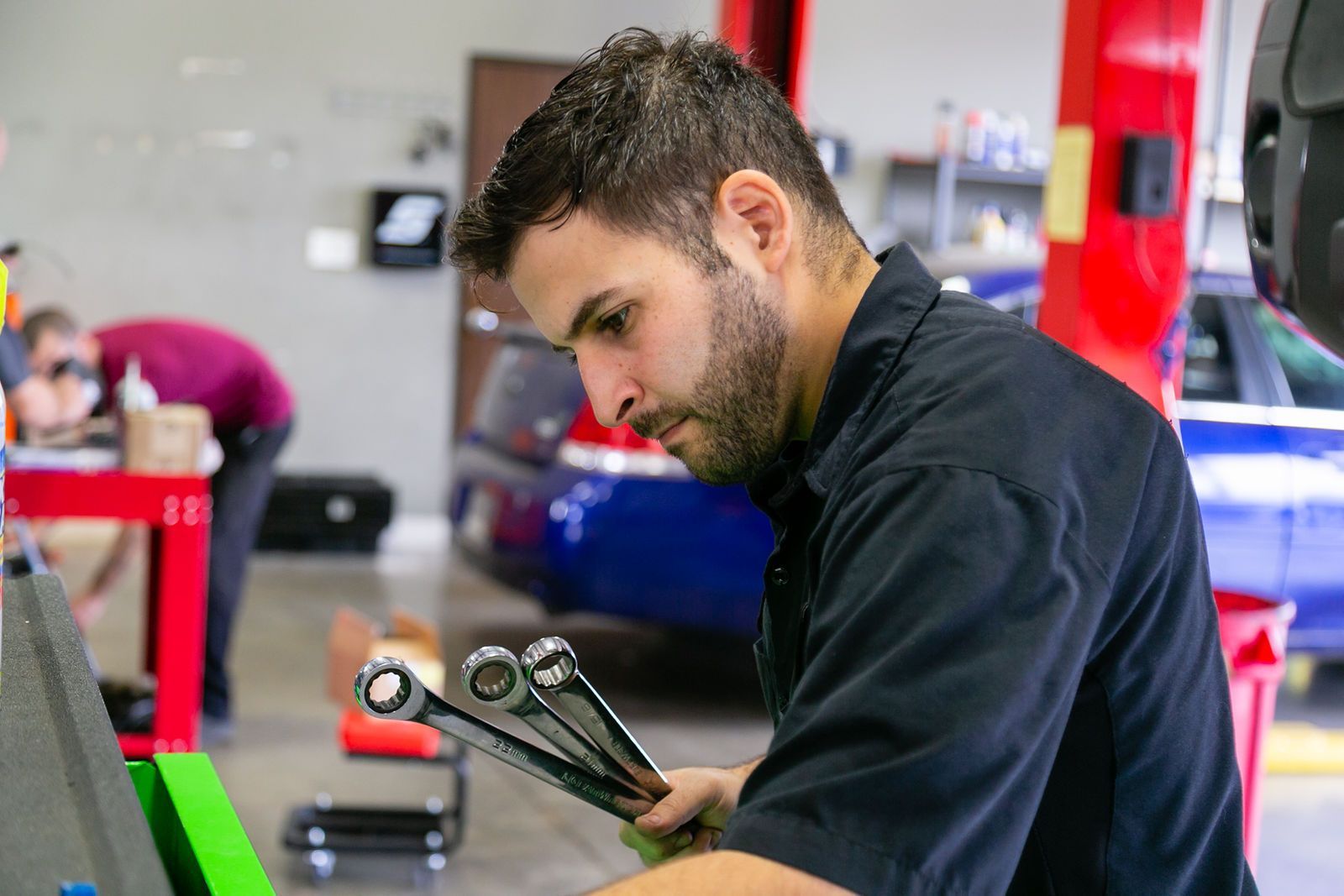 A mechanic in a black shirt holds several wrenches, focusing on his work inside an auto repair shop. | 2 QuickAuto, Car & Tire Repair | Copperfield
