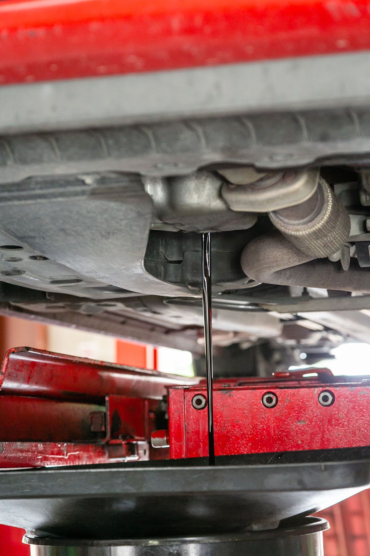 Used motor oil drains from the underside of a car into a black collection pan in an auto shop. | 2 QuickAuto, Car & Tire Repair | Copperfield