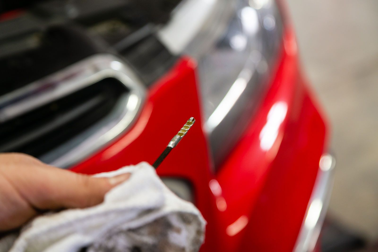 A person holding a clean car oil dipstick in front of the hood of a red car. | 2 QuickAuto, Car & Tire Repair | Copperfield