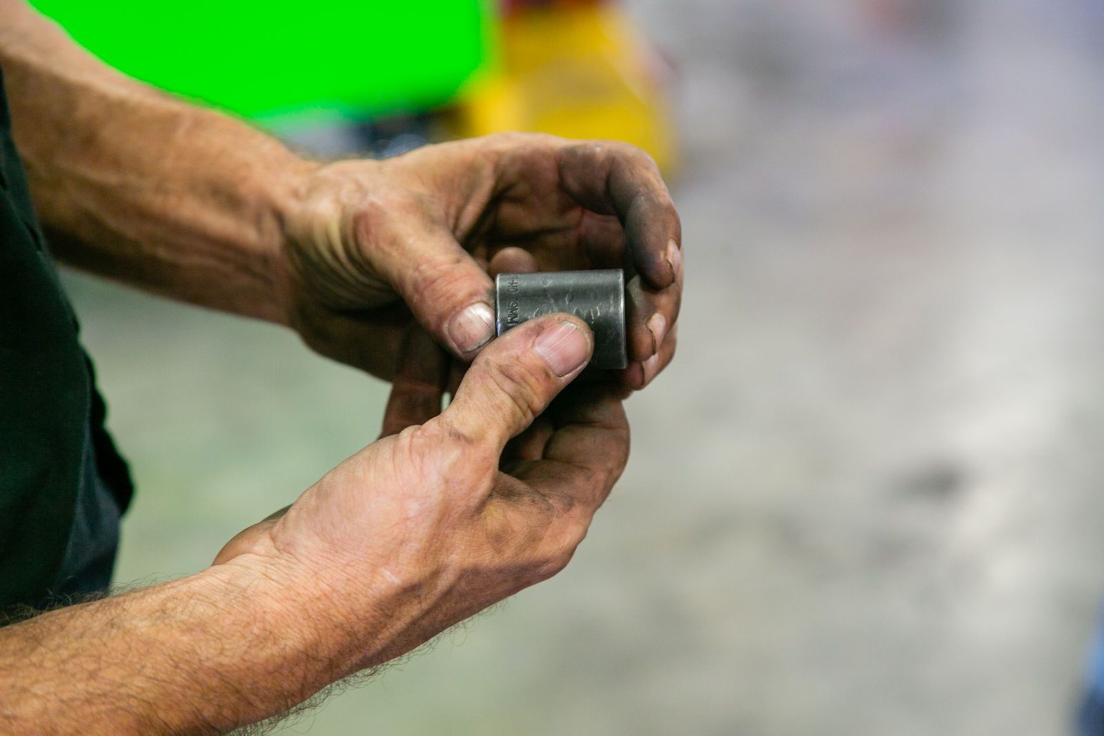 Hands with visible grime holding a small, gray cylindrical metal part, likely a machine component, in a workshop. | 2 QuickAuto, Car & Tire Repair | Copperfield