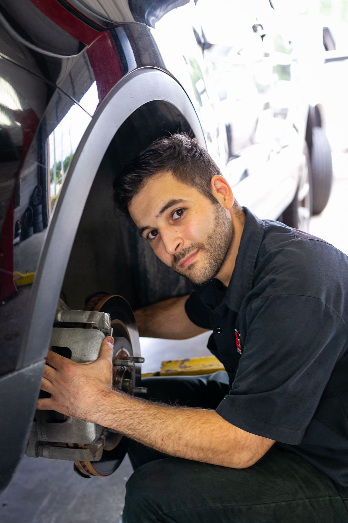 A person in a dark shirt inspecting the disc brakes inside the wheel well of a vehicle. | 2 QuickAuto, Car & Tire Repair | Copperfield