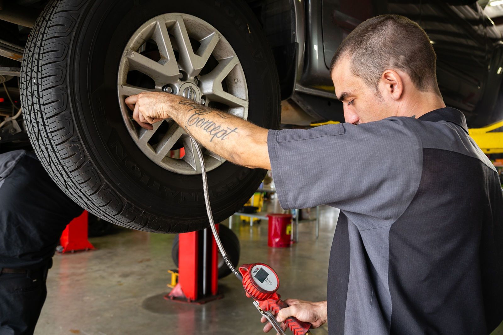 A mechanic in a garage uses a handheld pressure gauge to check the tire pressure on a raised vehicle. | 2 QuickAuto, Car & Tire Repair | Copperfield