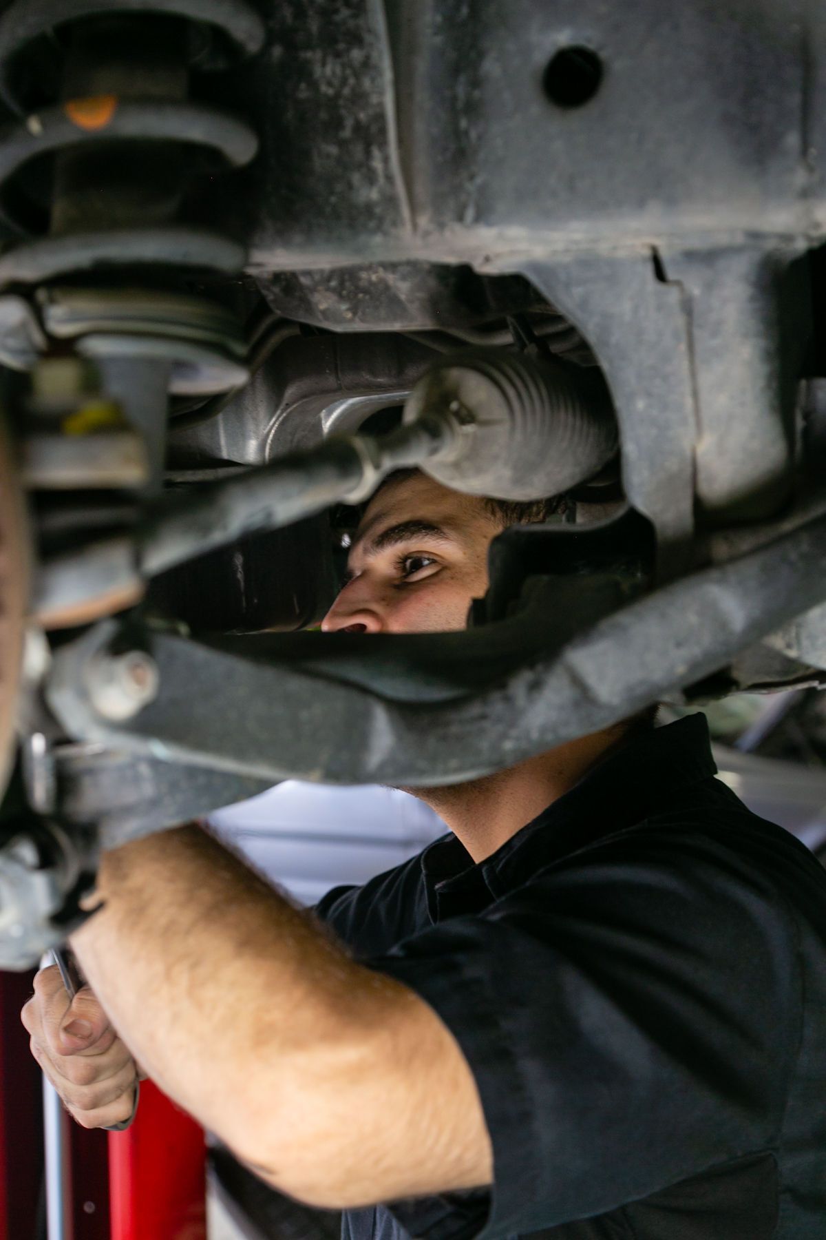 A mechanic in a black uniform works on the underside of a vehicle, focusing on the front suspension and steering components. | 2 QuickAuto, Car & Tire Repair | Copperfield