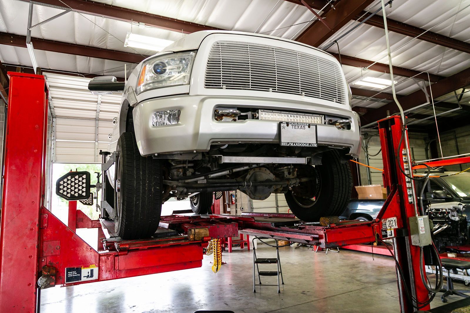 A white pickup truck elevated on a red four-post hydraulic car lift inside an auto repair shop. | 2 QuickAuto, Car & Tire Repair