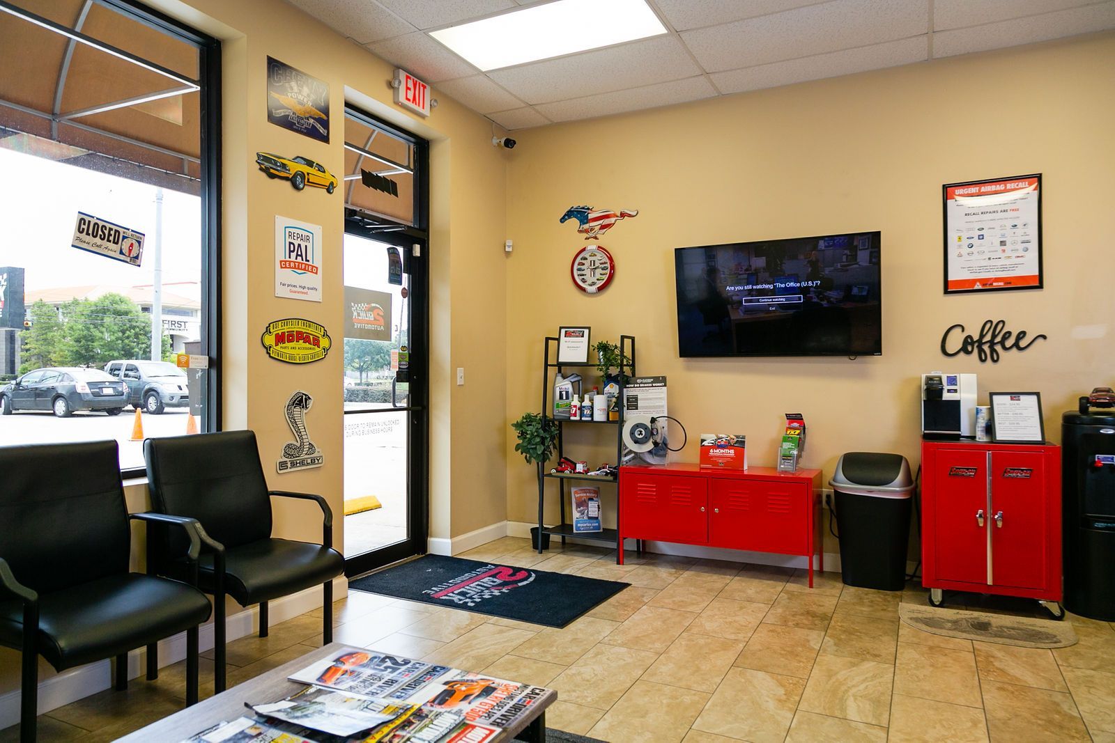 A waiting area with two black chairs, a television, a red cabinet, and automotive-themed wall signs. | 2 QuickAuto, Car & Tire Repair