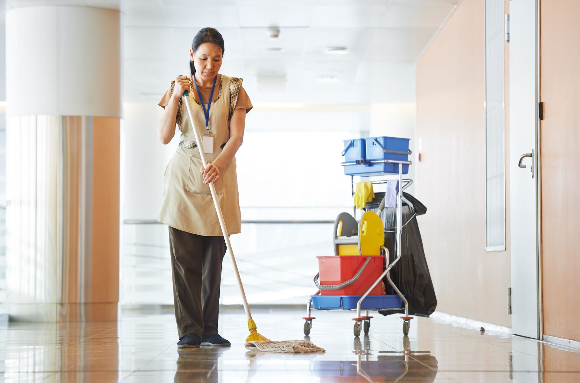 A woman is cleaning the floor with a mop in a hallway.