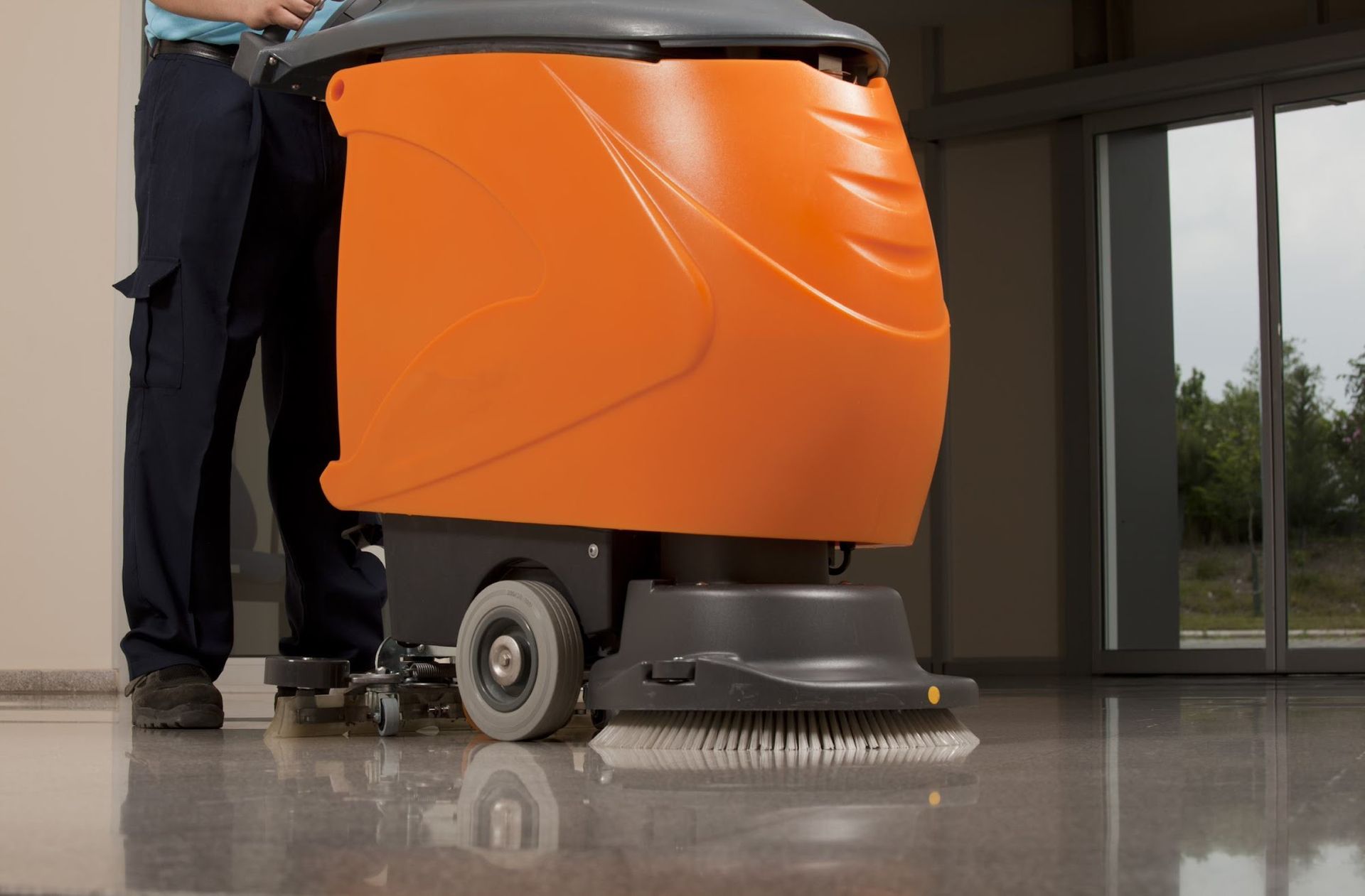 A man is cleaning the floor with an orange machine.