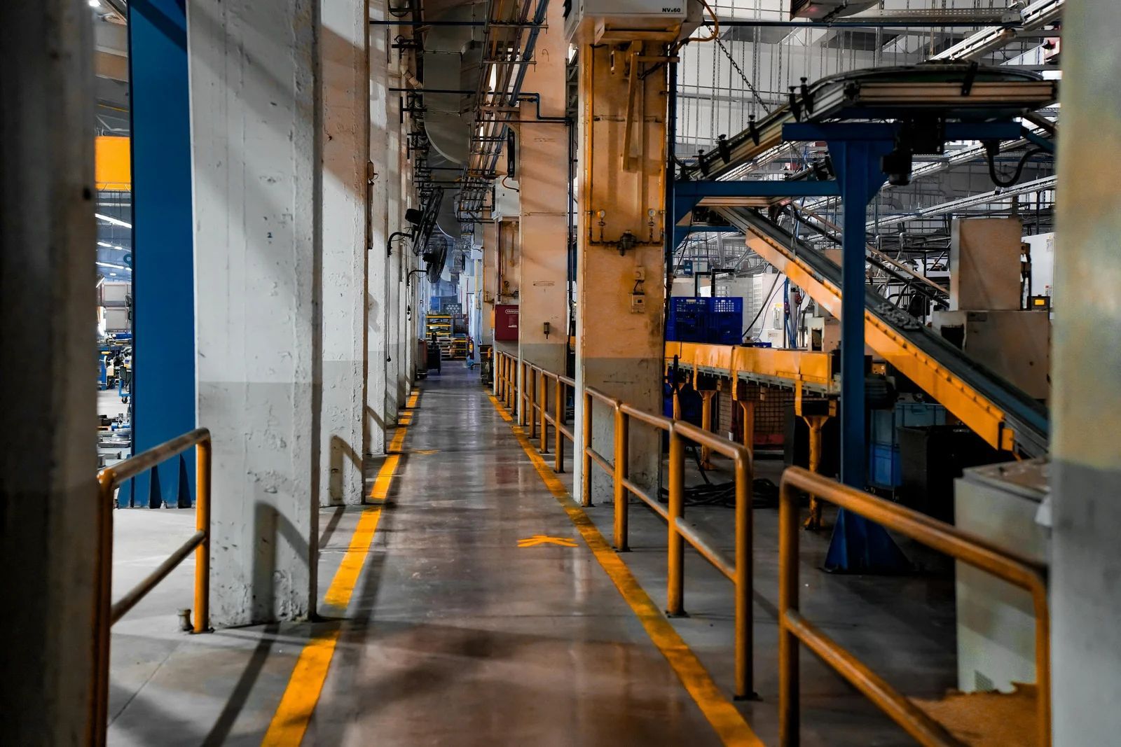 Long hallway in a factory, yellow handrails, conveyor belts, and machinery.