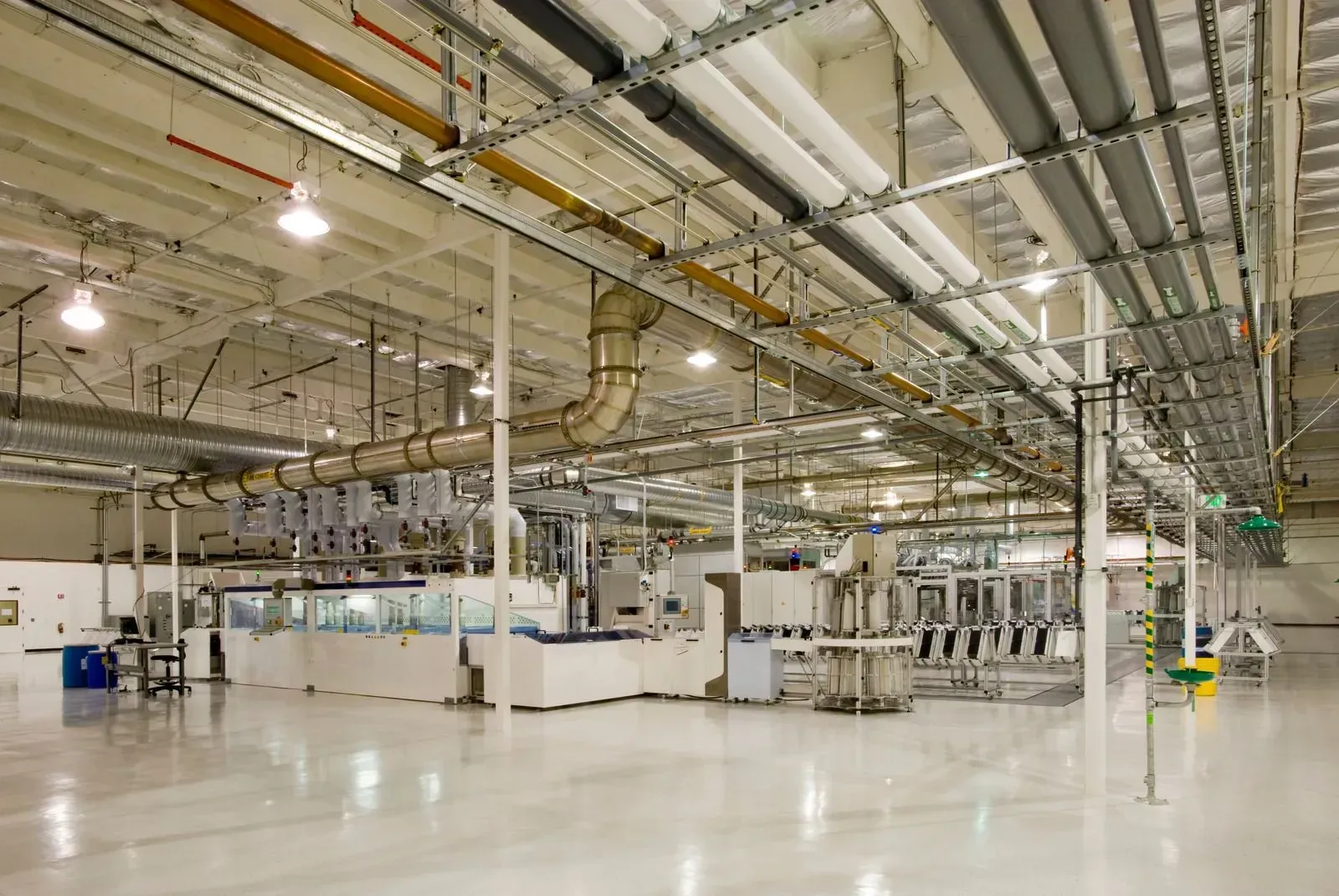 A large empty factory with lots of pipes hanging from the ceiling.