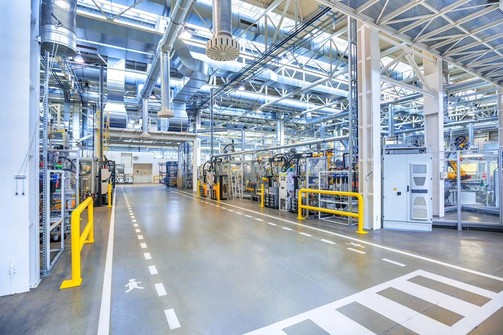 Spacious, modern industrial factory interior with automated machinery, yellow safety railings, and floor markings.