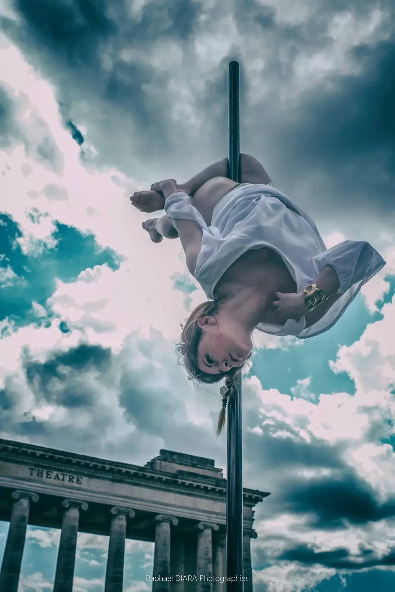 Une femme fait le poirier sur un poteau devant un immeuble.