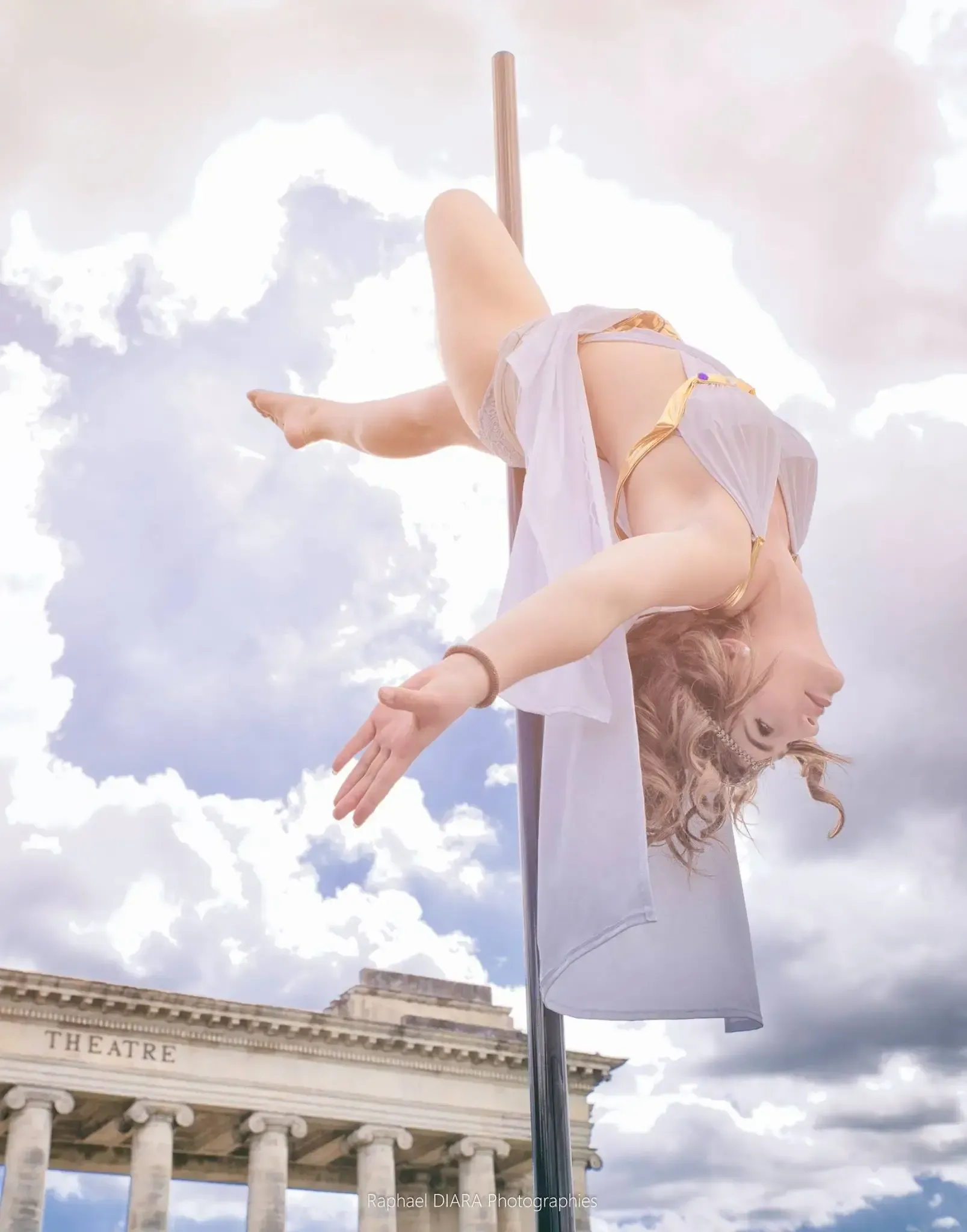Une femme fait des acrobaties aériennes sur un poteau devant un immeuble.