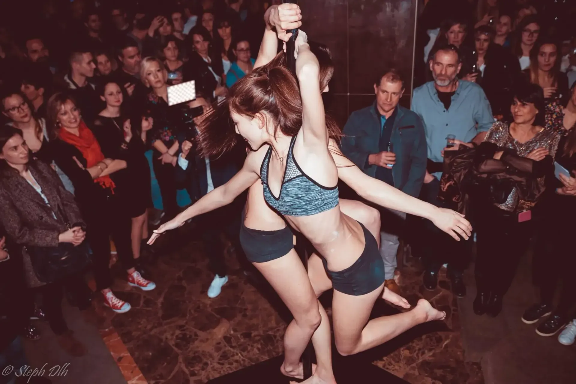 Deux danseurs de pole dance se produisent devant une foule de gens.