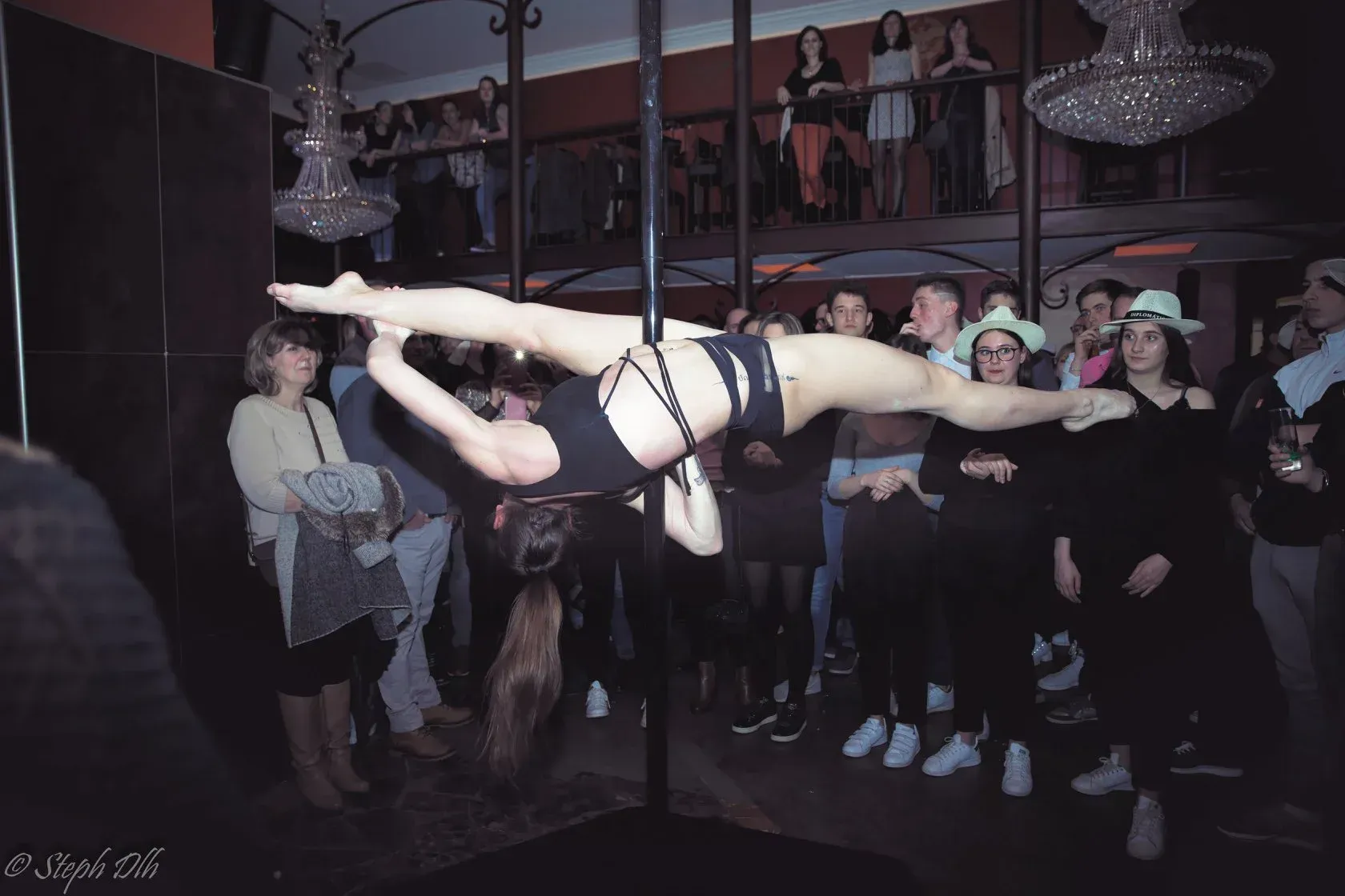 Une femme fait un grand écart sur un poteau devant une foule.